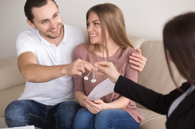 Jóvenes sonrientes propietarios de pareja consiguiendo llaves para poseer apartamento de casa