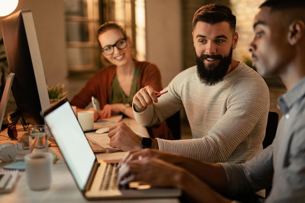 Foto gratuita jóvenes trabajadores independientes que usan una computadora portátil mientras trabajan hasta tarde en la oficina el foco está en el hombre con barba