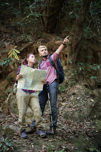 Jóvenes turistas pareja viajando en vacaciones en el bosque mirando el mapa en busca de atracciones. Concepto de viaje.