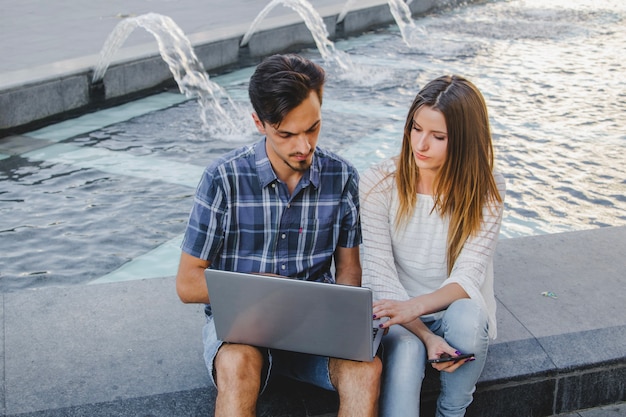 Foto gratuita jóvenes usando la computadora portátil en el parque