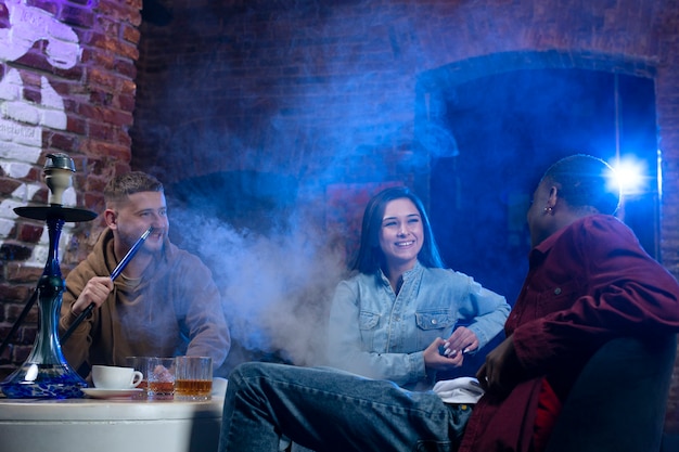 Foto gratuita jóvenes vapeando desde una pipa de agua en un bar.