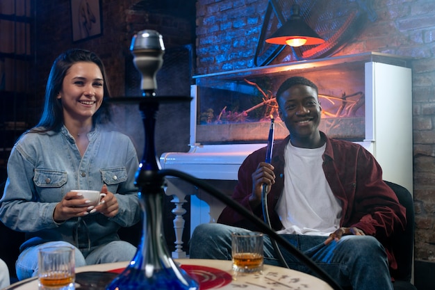 Foto gratuita jóvenes vapeando desde una pipa de agua en un bar.