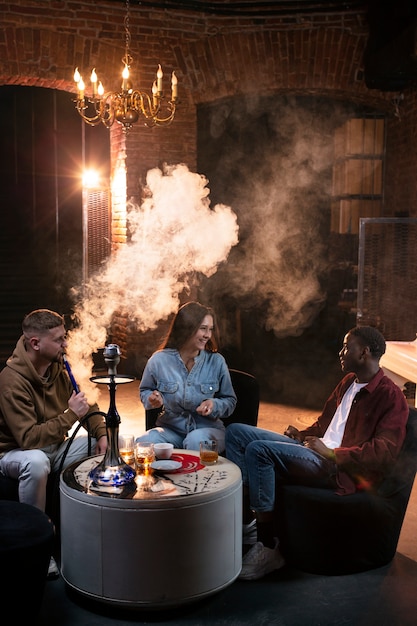 Foto gratuita jóvenes vapeando desde una pipa de agua en un bar.