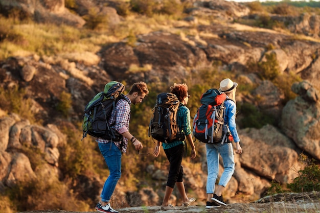 Jóvenes viajeros alegres con mochilas sonriendo, caminando en el cañón