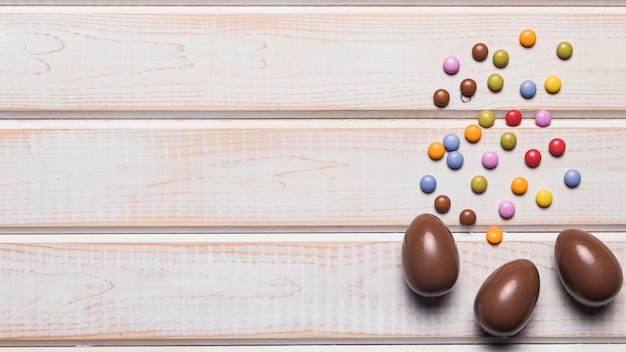 Foto gratuita joyas de caramelos multicolores y tres huevos de chocolate en superficie de madera