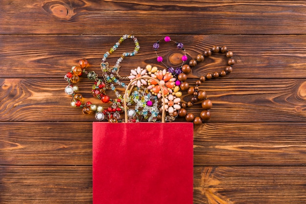 Joyas de cuentas y bolsa de papel rojo sobre fondo de madera