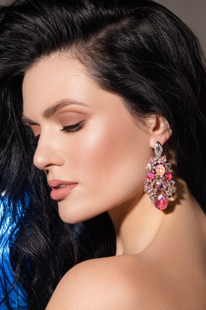 Joyería femenina con estilo. Retrato de hermosa mujer morena con aretes de brillo con maquillaje perfecto de cerca.