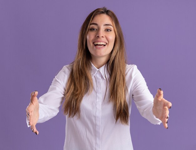 Joyful young pretty caucasian girl keeps hands open pretending to hold something on purple 
