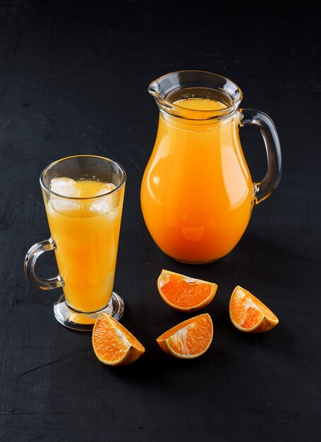Juce de naranja en vaso de vidrio y jarra con rodajas de naranja
