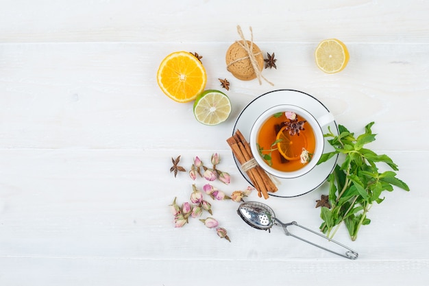 Juego de colador de té, hierbas, frutas cítricas y té de hierbas y galletas sobre una superficie blanca