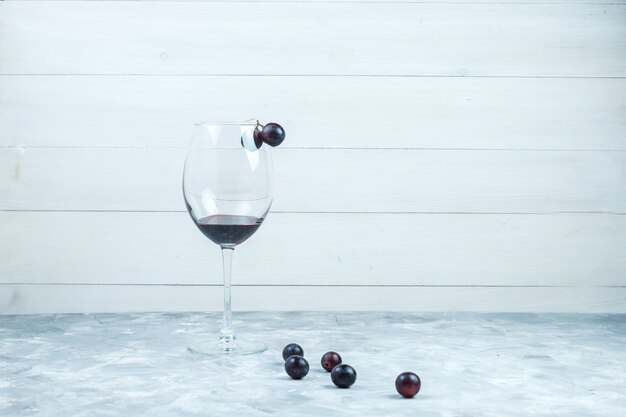 Juego de una copa de vino y uvas negras sobre fondo gris y madera sucio. vista lateral.