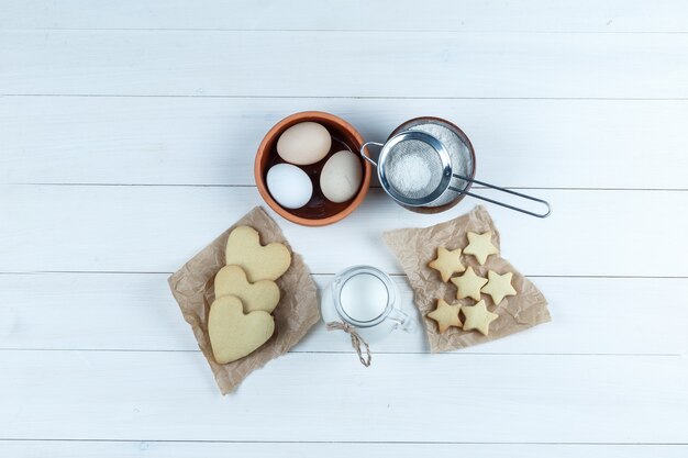 Juego de galletas, leche, azúcar en polvo y huevos en un recipiente sobre un fondo de madera. vista superior.