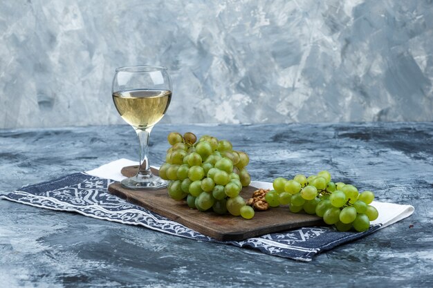 Juego de paño de cocina, vaso de whisky y uvas blancas sobre una tabla de cortar sobre un fondo de mármol azul claro y oscuro. de cerca.