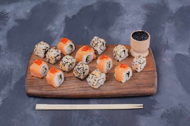 Foto gratuita juego de sushi. filadelfia y alaska rollos en placa de madera con palillos.