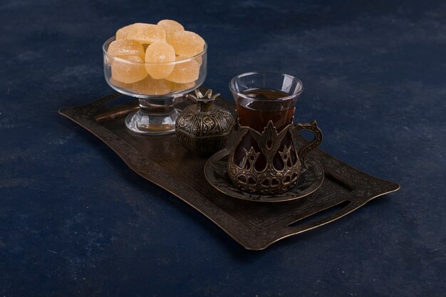 Juego de té con un vaso de té y mermeladas en bandeja metálica