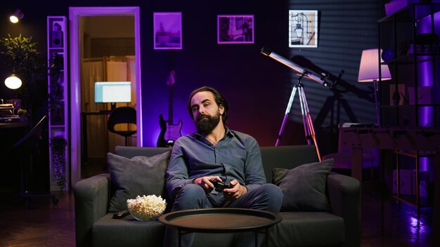 Jugador aburrido jugando en la consola de TV usando el gamepad comiendo palomitas de maíz