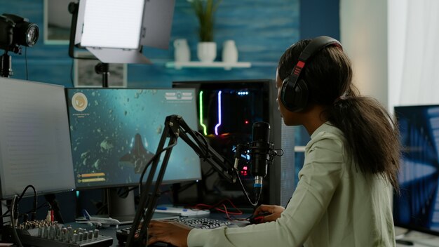 Jugador afro profesional de deportes electrónicos hablando por micrófono durante el torneo en vivo. Transmisión de videojuegos virales para ponerse los auriculares y escribir en el teclado durante el campeonato en línea.