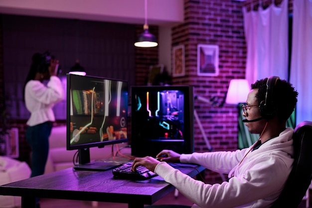 El jugador afroamericano que transmite videojuegos en línea juega en la PC, usa la computadora para divertirse con el torneo de juegos de esport. Jugador masculino jugando campeonato de juegos de acción en internet.