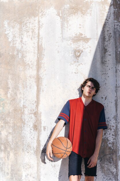 Jugador de baloncesto adolescente apoyado en la pared en un día soleado