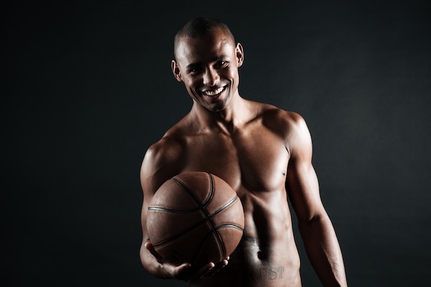 Jugador de baloncesto afroamericano joven sonriente que sostiene la bola