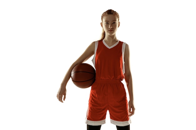 Foto gratuita jugador de baloncesto femenino caucásico joven que presenta confiado aislado en el fondo blanco. chica deportiva pelirroja. concepto de deporte, movimiento, energía y estilo de vida dinámico y saludable. entrenando, practicando.