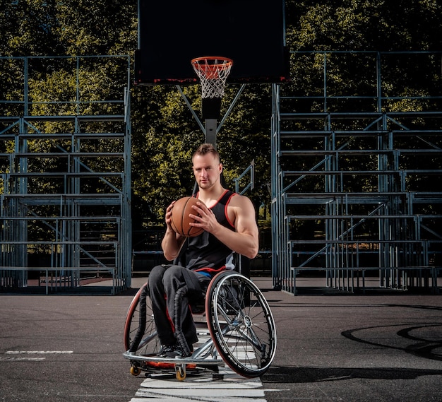 Un jugador de baloncesto lisiado en silla de ruedas sostiene una pelota en un campo de juego abierto.