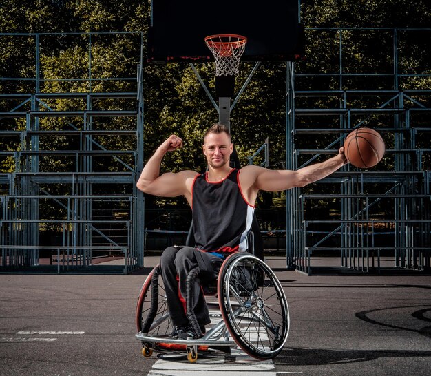 Un jugador de baloncesto lisiado sonriente en silla de ruedas sostiene una pelota en un terreno de juego abierto.