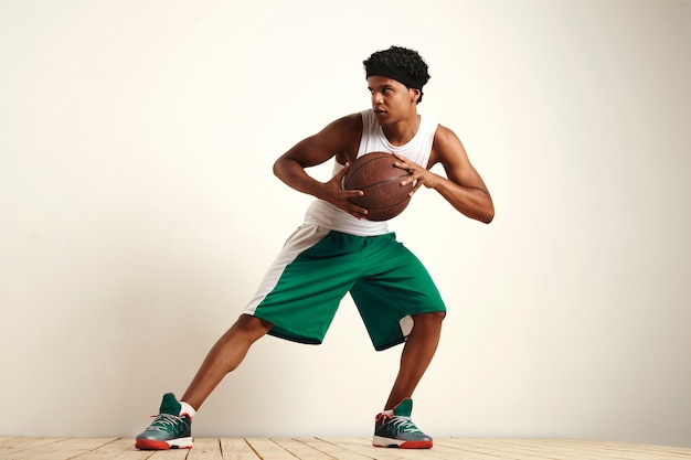 Jugador de baloncesto profesional practicando la defensa con una vieja pelota de baloncesto de cuero aislado en blanco