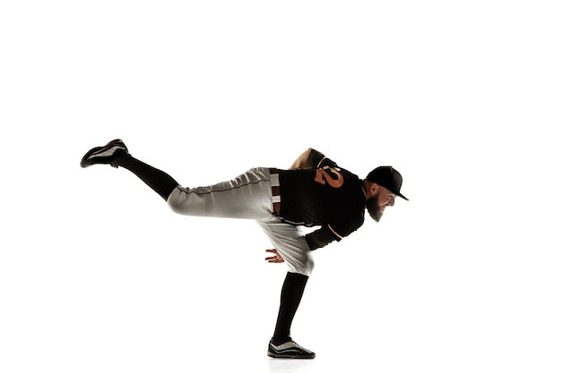 Foto gratuita jugador de béisbol, lanzador con uniforme negro practicando y entrenando aislado en una pared blanca. joven deportista profesional en acción y movimiento. estilo de vida saludable, deporte, concepto de movimiento.