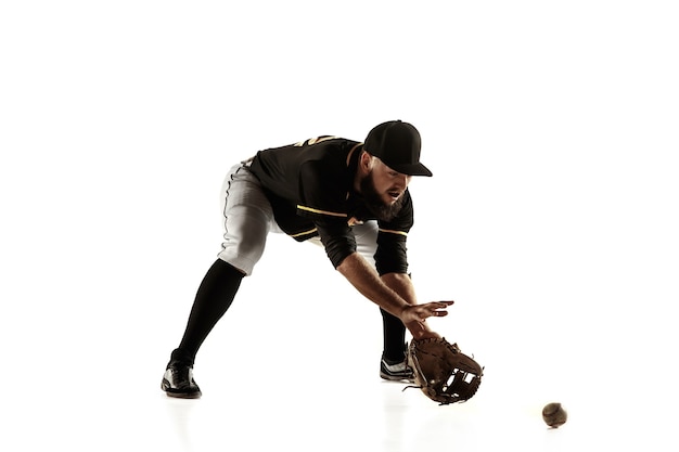 Jugador de béisbol, lanzador con uniforme negro practicando y entrenando aislado en una pared blanca. Joven deportista profesional en acción y movimiento. Estilo de vida saludable, deporte, concepto de movimiento.