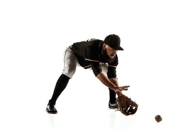 Jugador de béisbol, lanzador con uniforme negro practicando y entrenando aislado en una pared blanca. Joven deportista profesional en acción y movimiento. Estilo de vida saludable, deporte, concepto de movimiento.