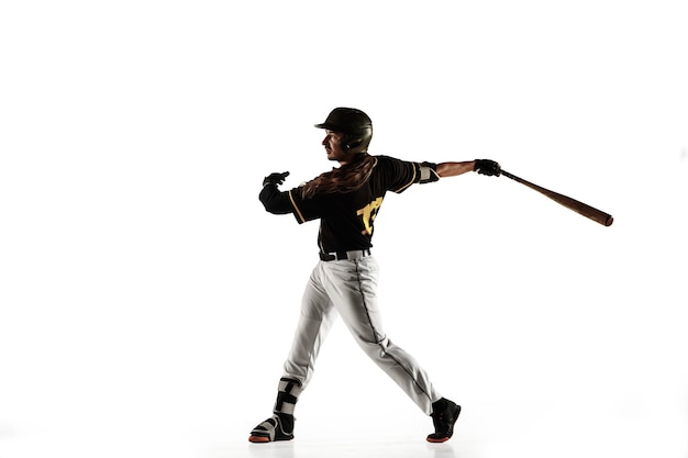 Jugador de béisbol, lanzador con uniforme negro practicando y entrenando aislado en una pared blanca. Joven deportista profesional en acción y movimiento. Estilo de vida saludable, deporte, concepto de movimiento.