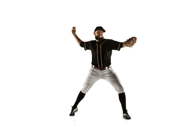 Jugador de béisbol, lanzador con uniforme negro practicando y entrenando aislado en una pared blanca. Joven deportista profesional en acción y movimiento. Estilo de vida saludable, deporte, concepto de movimiento.