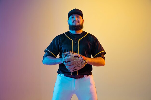 Jugador de béisbol, lanzador con uniforme negro practicando y entrenando sobre fondo degradado con luz de neón