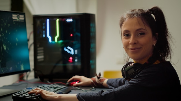 Jugador concentrado mirando a la cámara mientras juega un videojuego en línea de disparos espaciales en una poderosa computadora personal RGB durante el campeonato de egames. Esport cyber actuando durante el torneo de juegos