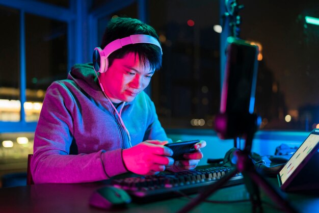 Jugador de esports masculino asiático que juega juegos multijugador de ligas deportivas en línea a través de un teléfono inteligente con auriculares emocionados y alegres que usan hombres asiáticos que juegan juegos de teléfonos inteligentes en línea junto con amigos