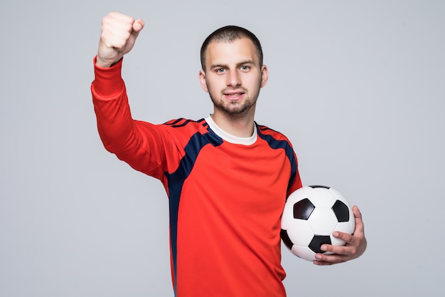 Jugador de fútbol emocionado en camiseta roja sosteniendo un concepto de victoria de fútbol aislado en blanco