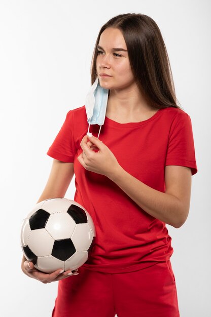 Foto gratuita jugador de fútbol femenino con máscara sosteniendo bola