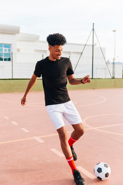 Jugador de fútbol negro corriendo y pateando la pelota en el campo de deportes