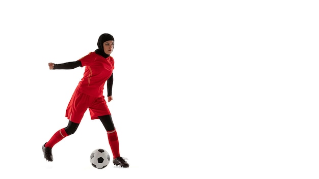Jugador de fútbol o fútbol femenino árabe aislado sobre fondo blanco de estudio. Mujer joven pateando la pelota, entrenamiento en movimiento, acción. Flyer, doble techo.