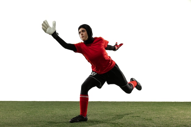 Jugador de fútbol o fútbol femenino árabe, portero sobre fondo blanco de estudio. Mujer joven atrapando pelota, entrenando, protegiendo goles en movimiento y acción. Concepto de deporte, afición, estilo de vida saludable.