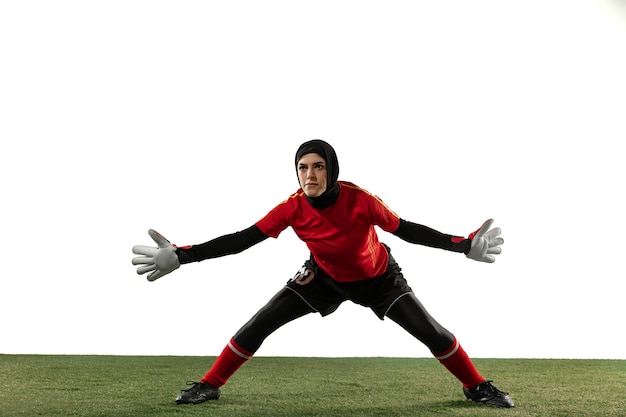 Jugador de fútbol o fútbol femenino árabe, portero sobre fondo blanco de estudio. Mujer joven atrapando pelota, entrenando, protegiendo goles en movimiento y acción. Concepto de deporte, afición, estilo de vida saludable.