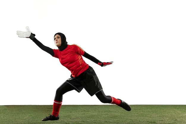 Jugador de fútbol o fútbol femenino árabe, portero sobre fondo blanco de estudio. Mujer joven atrapando pelota, entrenando, protegiendo goles en movimiento y acción. Concepto de deporte, afición, estilo de vida saludable.