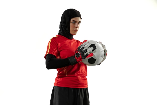 Jugador de fútbol o fútbol femenino árabe, portero sobre fondo blanco de estudio. Mujer joven posando confiada con balón, protegiendo goles para el equipo.