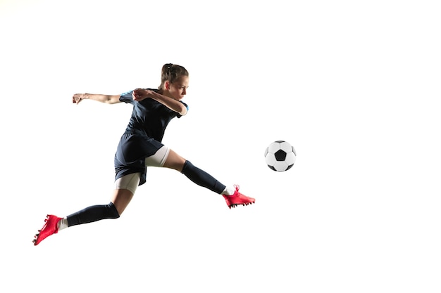 Jugador de fútbol o fútbol femenino joven con el pelo largo en ropa deportiva y botas pateando la pelota para el gol en salto aislado sobre fondo blanco. Concepto de estilo de vida saludable, deporte profesional, afición.