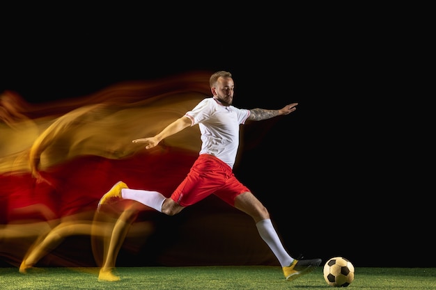 Jugador de fútbol o fútbol masculino caucásico joven en ropa deportiva y botas pateando la pelota