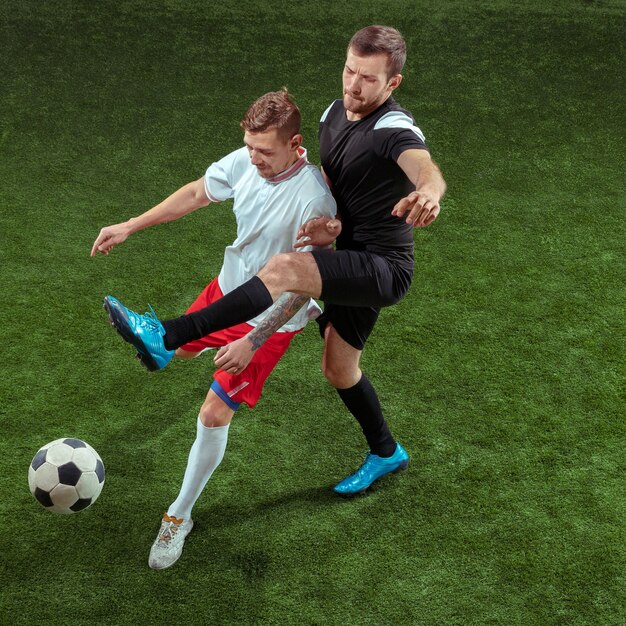 Jugador de fútbol que aborda la pelota sobre fondo de hierba verde. Jugadores de fútbol masculinos profesionales en movimiento en el estadio. Montar hombres saltadores en acción, salto, movimiento en el juego.