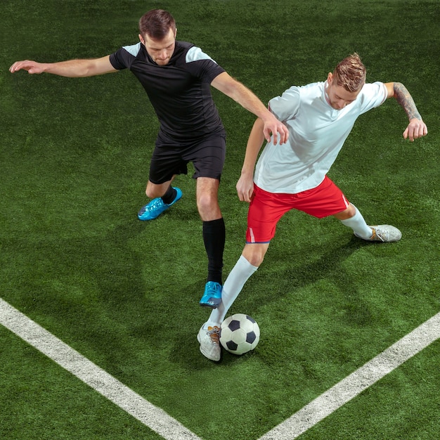 Jugador de fútbol que aborda la pelota sobre fondo de hierba verde. Jugadores de fútbol masculinos profesionales en movimiento en el estadio. Montar hombres saltadores en acción, salto, movimiento en el juego.