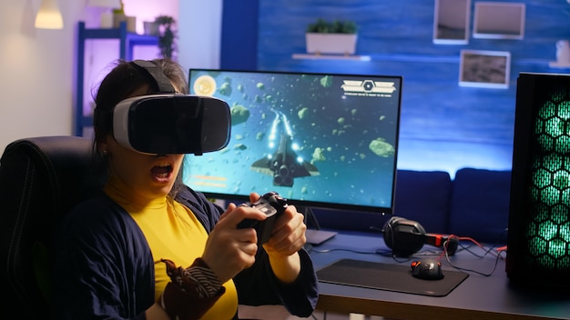 Jugador ganador con gafas de realidad virtual, jugando videojuegos de disparos espaciales en la habitación con RGB