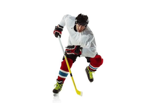 Jugador de hockey masculino joven con el palo en la cancha de hielo y pared blanca. Deportista con equipo y casco practicando acción.